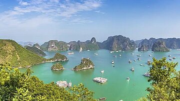 Blick über die Halong‑Bucht: Karstfelsen ragen aus grünem Wasser, Boote zwischen den Inseln.