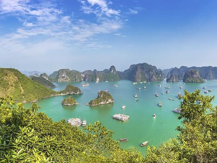 Blick über die Halong‑Bucht: Karstfelsen ragen aus grünem Wasser, Boote zwischen den Inseln.