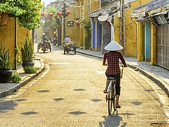 Radfahrer mit Sonnenhut fährt durch die Gassen der Altstadt von Hoi An.