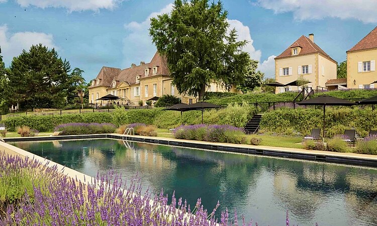 Blick auf Château les Merles: Sandsteingebäude, Garten mit Lavendel und Pool.