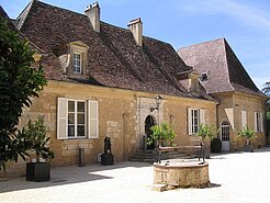 Historische Fassade und Innenhof von Château les Merles mit Brunnen und hellen Fensterläden.